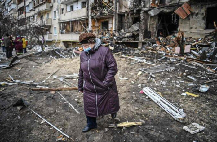 Anziana signora cammina tra i resti si un bombardamento in una città